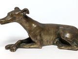 bronze statue of a dog laying down on a white surface
