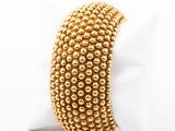 a close up of a gold beaded bracelet on a white surface