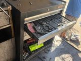 un homme debout à côté d'un barbecue contenant des ustensiles