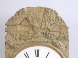 a gold clock with a picture of a village on it
