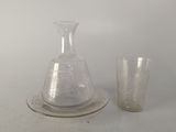 un verre et une carafe posés sur une assiette, à côté d'un verre à pied
