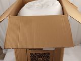 une boîte en carton contenant un oreiller, posée sur un lit