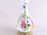 un vase blanc orné de fleurs peintes, posé sur un socle doré