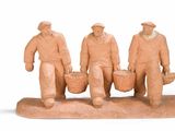 trois figurines représentant des hommes portant des paniers, posées sur une surface blanche