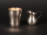 two silver cups and a silver pitcher on a black surface