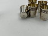 four silver shot glasses sitting next to each other on a white surface