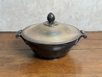 une cocotte ancienne en métal argenté avec son couvercle, posée sur une table en bois