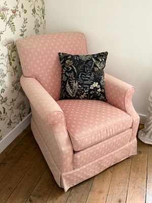 une chaise rose avec un coussin posé dessus, dans un coin de la pièce