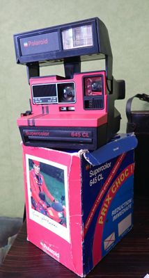 un appareil photo Polaroid rose posé sur une pile de cartons