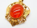 une photo d'un pendentif plaqué or orné d'une pierre en verre rouge taillée en cabochon