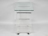 a clear glass side table with three shelves on casteors