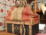 une petite valise posée sur une table, avec une poupée en arrière-plan