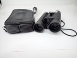 un sac noir et une paire de jumelles posés sur une table blanche