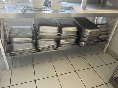 Plusieurs casseroles sont empilées sur une étagère en acier inoxydable dans une cuisine.