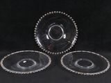trois plats en verre transparent aux bords perlés, posés sur un fond noir