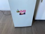 a small white refrigerator in a kitchen with a cutting board on the counter