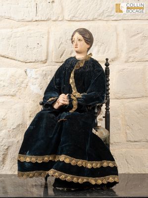 a statue of a woman sitting on a chair in front of a stone wall