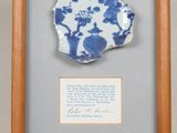 une vieille assiette bleue et blanche, encadrée dans un cadre en bois, sur laquelle est inscrit un poème