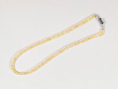 collier composé de perles jaunes et blanches, orné d'une fleur verte sur fond blanc