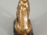 bronze statue of a dog sitting on a rock on a white surface