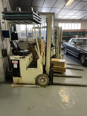 un chariot élévateur dans un entrepôt, avec une voiture en arrière-plan
