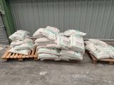 Plusieurs sacs de ciment sont posés sur des palettes devant un bâtiment