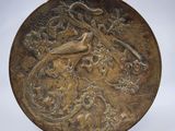 une plaque en bronze ornée d'un oiseau et de fleurs