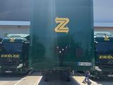 several large green trucks parked in a parking lot with a person sitting on the ground