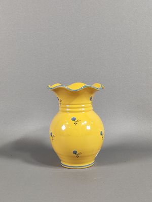 un vase jaune orné de fleurs bleues, posé sur un fond gris