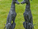 two statues of greyhound dogs sitting on top of each other in the grass