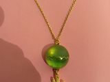 a gold necklace with a green glass bead and a cactus on it