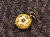 une petite montre de poche en or posée sur un tissu marron