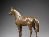 bronze statue of a horse on a wooden base against a gray background