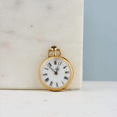 une petite montre de poche en or posée sur un bloc de marbre