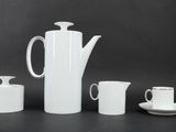 a white coffee pot, cups and saucer on a table