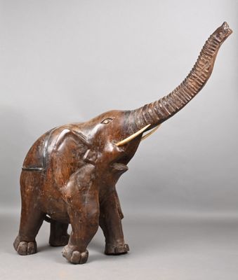 carved wooden elephant with tusks and tusks standing on a gray surface