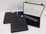 three black leather cases with red linings are on a white surface