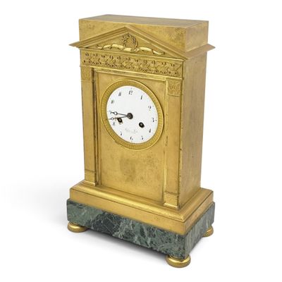 une horloge dorée posée sur un socle en marbre, sur fond blanc