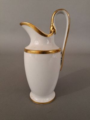 a white and gold pitcher with a handle on a table