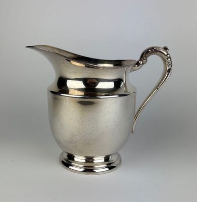 an antique silver plated pitcher with a curved handle