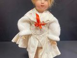a close up of a doll with blonde hair wearing a white dress and a red bow