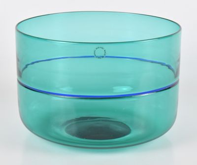 un bol en verre vert à bord bleu posé sur une surface blanche