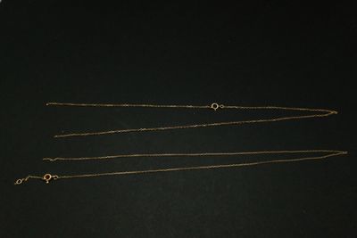 trois colliers en or posés sur une surface noire, sur fond noir