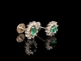 une paire de boucles d'oreilles en émeraude et diamant posées sur un fond noir