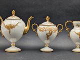 three white and gold vases and a teapot sitting on a table