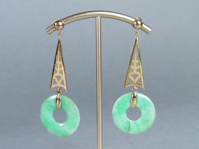 paire de boucles d'oreilles en jade vert et or, posées sur un support en métal