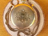 a silver pocket watch with a chain around it on a piece of wood