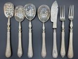 six cuillères et un couteau en métal argenté sont alignés sur un fond gris