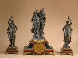 three statues of women with a clock on top of a table