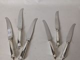 four silver plated knives with handles on a white surface